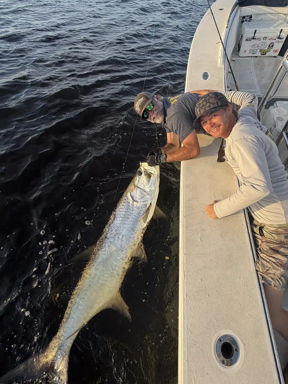 Two anglers beside a large tarpon at the side of a fishing boat near Sarasota, Florida.